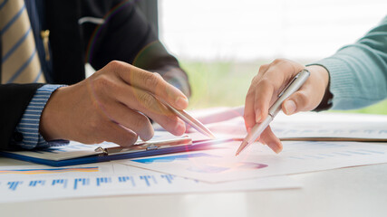 Business team discussing and planning projects using charts, holding pens and analytical papers on office table. with a laptop computer and a financial graph running in the background. business idea