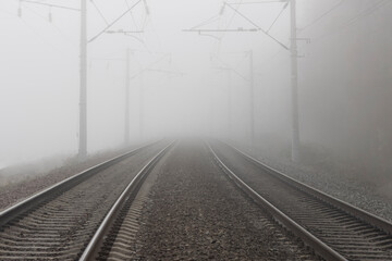 A railroad going into fog in the middle of an autumn landscape. Rails lost in the distance and disappearing into the fog.