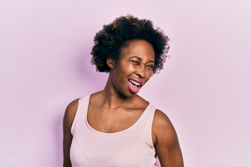 Young african american woman wearing casual sleeveless t shirt winking looking at the camera with...