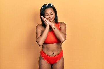 Young african american girl wearing bikini sleeping tired dreaming and posing with hands together while smiling with closed eyes.