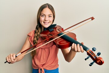 Beautiful brunette little girl playing violin smiling and laughing hard out loud because funny...