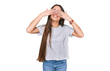 Young hispanic girl wearing casual white t shirt covering eyes with hands smiling cheerful and funny. blind concept.