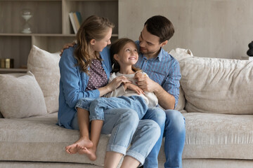 Caring bonding happy millennial couple parents holding on laps sincere cute small child daughter,...