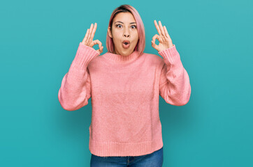 Hispanic woman with pink hair wearing casual winter sweater looking surprised and shocked doing ok approval symbol with fingers. crazy expression