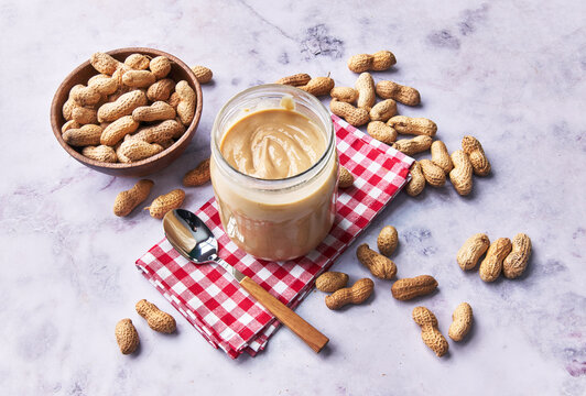  Bowl of peanuts with shell and peanut butter cream on a marble surface