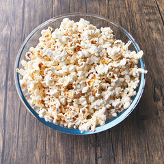  Bowl of salty popcorns on a wooden surface