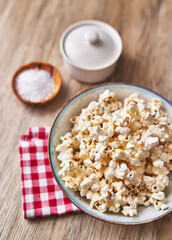  Bowl of salty popcorns on a wooden surface