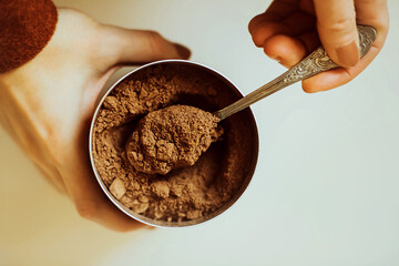 A woman in a brown jacket holds a jar of fragrant cocoa powder in her hands and takes out a portion...