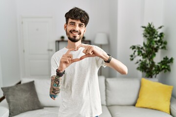 Hispanic man with beard at the living room at home smiling in love doing heart symbol shape with hands. romantic concept.
