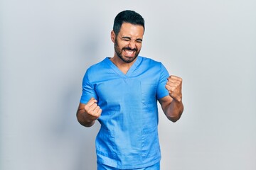 Handsome hispanic man with beard wearing blue male nurse uniform very happy and excited doing...