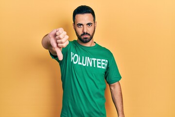 Handsome hispanic man with beard wearing volunteer t shirt with angry face, negative sign showing dislike with thumbs down, rejection concept