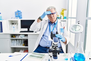 Fototapeta premium Senior caucasian man working at scientist laboratory worried and stressed about a problem with hand on forehead, nervous and anxious for crisis