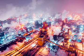 Aerial view of steel plant at night with smokestacks and fire blazing out of the pipe. Industrial panoramic landmark with blast furnance of metallurgical production. Concept of environmental pollution