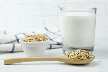 Oatmeal in a wooden spoon, a glass of milk and tea towel on light background. Healthy food concept, oat milk, food for allergy sufferers and vegetarians. Selective focus on spoon, blurred background.