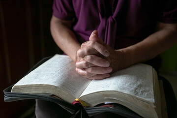 Close up view of senior woman hands on open bible, folded in prayer.