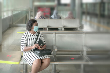 Businesswoman wearing medical face mask holding a smartphone, sitting and waiting at subway station. Masked transit concept.