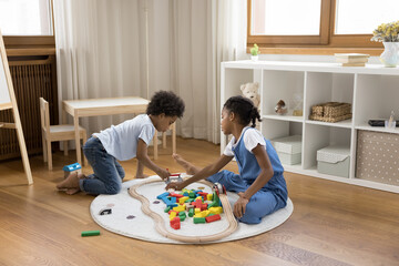 Two Black little sibling children sitting on floor at home, playing with wooden colorful toy...