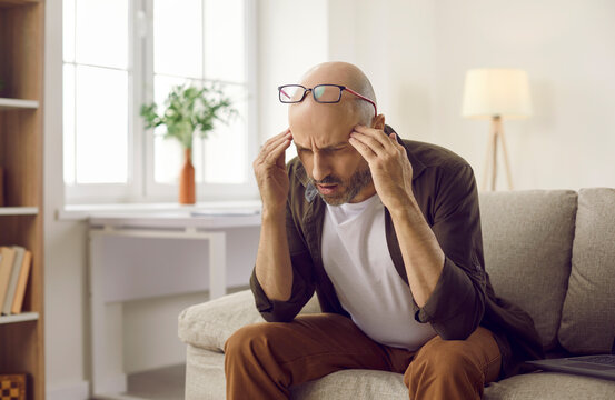 Man starts to realise. Confused thinker sitting on sofa with laptop computer at home, thinking, trying to understand situation, find answer, remember difficult word, analyze or resolve complex problem