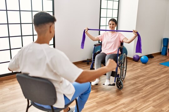 Young disabled woman sitting on wheelchair making mobility exercise using elastic band at the clinic.