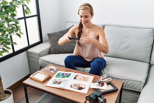 Young caucasian woman making picture to photo book sitting on sofa at home
