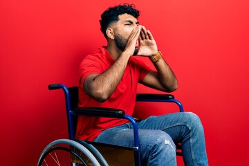 Fototapeta na wymiar Arab man with beard sitting on wheelchair shouting angry out loud with hands over mouth