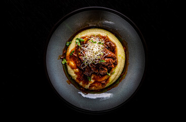 Stewed veal cheeks with mashed potatoes on plate on rustic wooden table dark background
