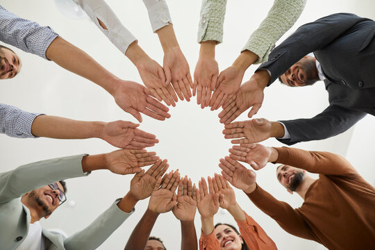 Group of happy diverse people joining hands. Mixed race team of different smiling young people putting hands together, cropped shot from below. Teamwork, community, help, support, volunteering concept
