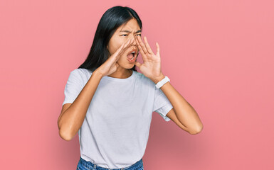 Beautiful young asian woman wearing casual white t shirt shouting angry out loud with hands over mouth