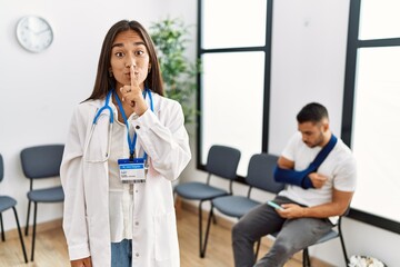 Fototapeta premium Young asian doctor woman at waiting room with a man with a broken arm asking to be quiet with finger on lips. silence and secret concept.