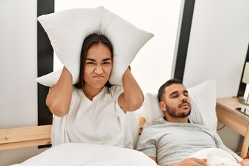 Woman covering ears with pillow irritated for snore lying in bed at home.