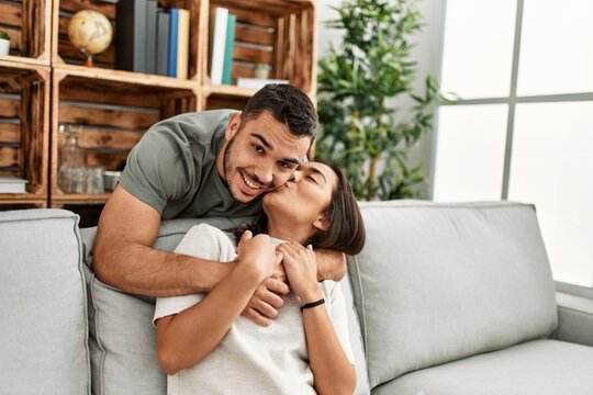 Young latin couple sitting on the sofa hugging at home.