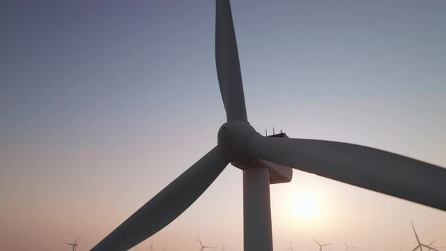 Close-up of wind turbine blades at sunset or sunrise. Windmills with rotating wings among green fields. Technology for wind energy, renewable energy source, earth care. Wind power station, drone video
