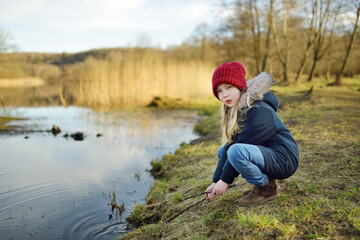 Cute young girl having fun by a river on warm spring day. Child playing by a water.