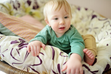 Adorable baby boy sitting in a chair by the window.