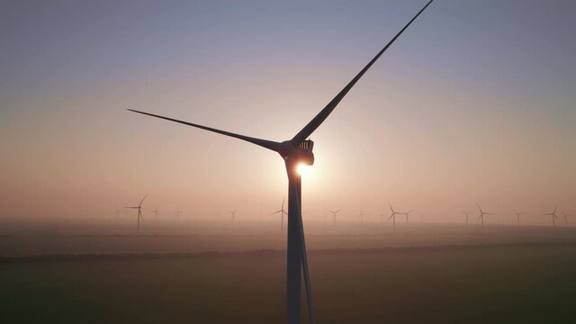 Close-up of wind turbine blades at sunset or sunrise. Windmills with rotating wings among green fields. Technology for wind energy, renewable energy source, earth care. Wind power station, drone video