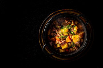 Goulash. Vegetable rague with meat, eggplant, pepper, potato and carrot in black bowl on dark wooden background