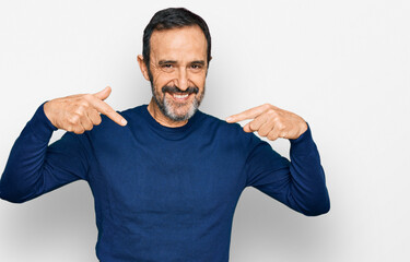 Middle age hispanic man wearing casual clothes looking confident with smile on face, pointing...