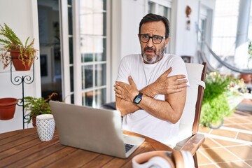 Middle age man using computer laptop at home shaking and freezing for winter cold with sad and shock expression on face