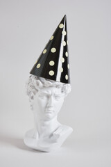replica bust of king david in a festive cardboard hat on a gray background, new year concept,...
