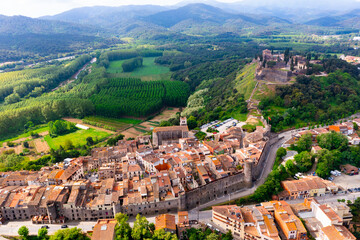 View from drone of Spanish village of Hostalric overlooking ancient Parish church of Santa Maria and fortified castle on hilltop on sunny summer day, province of Girona