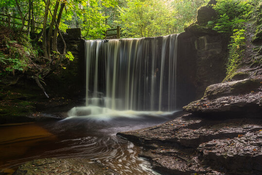 Epic beautiful Autumn landscape image of Nant Mill waterfall in Wales with glowing sunlight through the woodland