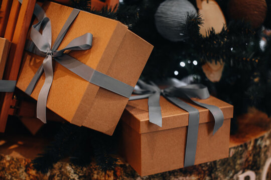 Paper beige New Year's gift with grey ribbon under the Christmas tree. Festive holiday concept and presents