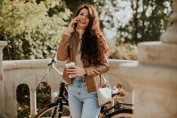 Fototapeta na wymiar Young woman with mobile phone drink coffee to go by the bicycle on autumn day