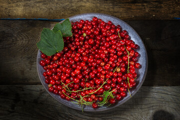 Red currants in a bowl on a black background. Berries from the village garden. Wooden vintage table