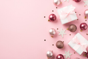 Top view photo of pink christmas decorations balls snowflakes confetti and white gift boxes with pink ribbon bows on isolated pastel pink background with copyspace