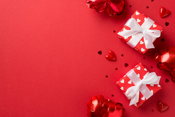 Top view photo of valentine's day decorations white gift boxes with red ribbon bows heart shaped balloons and confetti on isolated red background with empty space