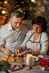 Family christmas tradition woman and man aged to cook gingerbread cookies at home kitchen, vertical photo