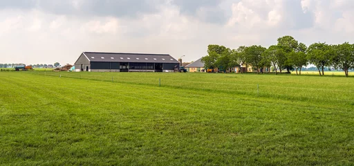 Deurstickers Moderne Hollandse boerderij met veel grasland in de provincie Noord-Brabant. De foto is genomen op een licht bewolkte dag aan het einde van het lenteseizoen. © Ruud Morijn