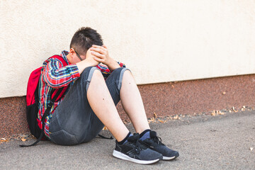 Lonely boy sitting alone on the ground, isolated from his peers, hiding