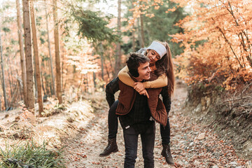 Naklejka na ściany i meble Young romantic couple in the woods. Piggyback riding. Happy together